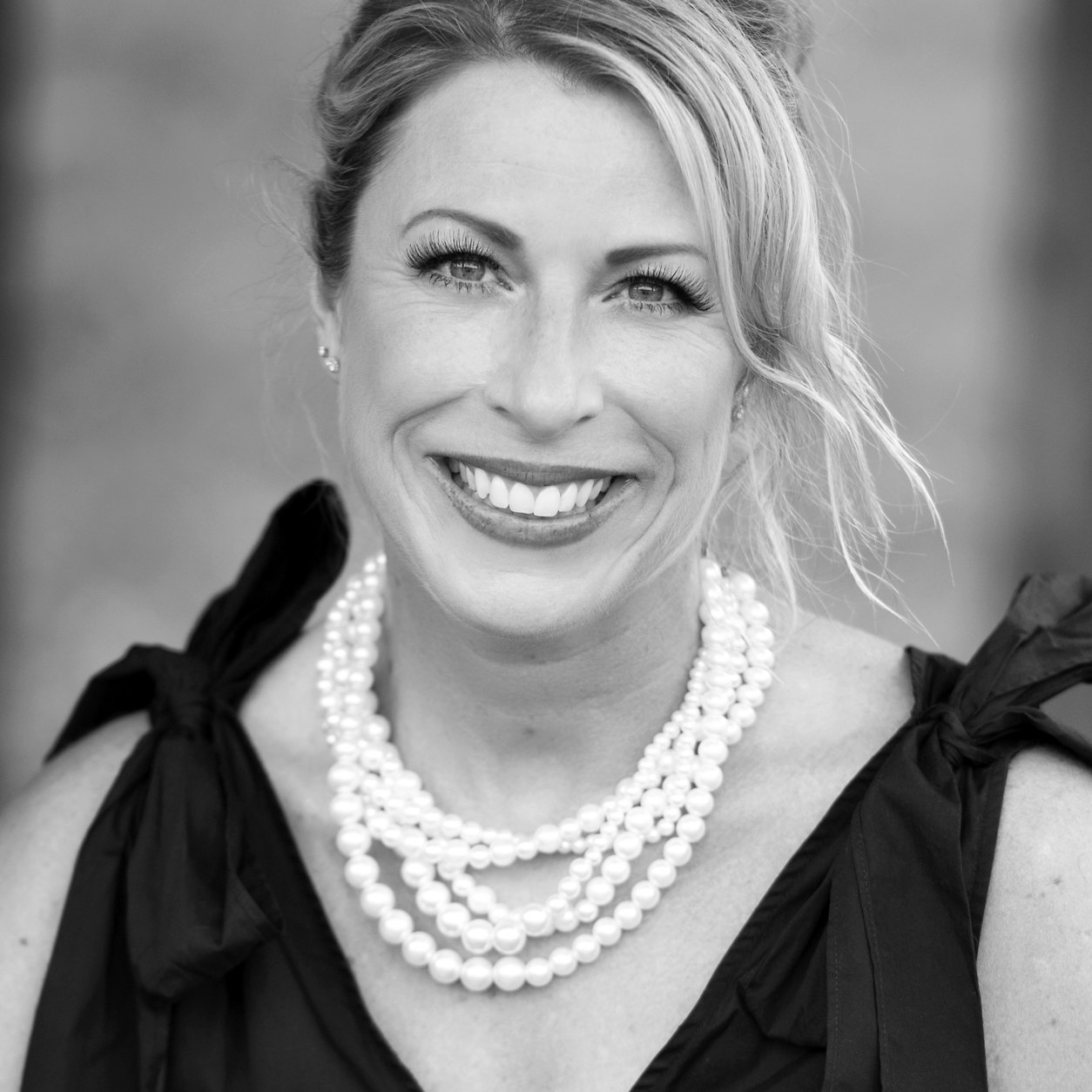 Abbey Robertson smiling, in a black dress with a layered pearl necklace