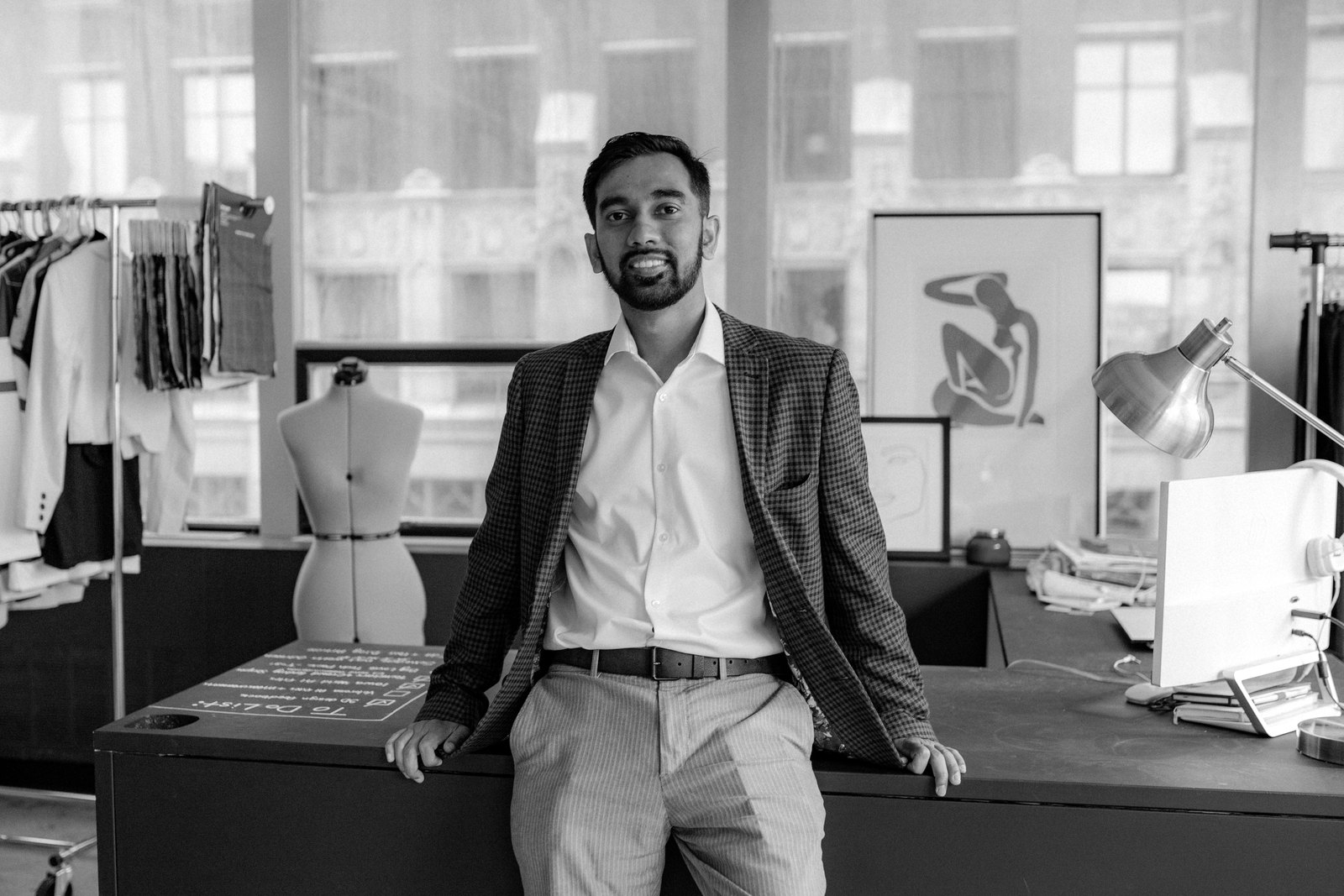 Russel Karim, CEO of SourceEazy, in a checked blazer leaning on a design table in a studio with garment racks and a dress form