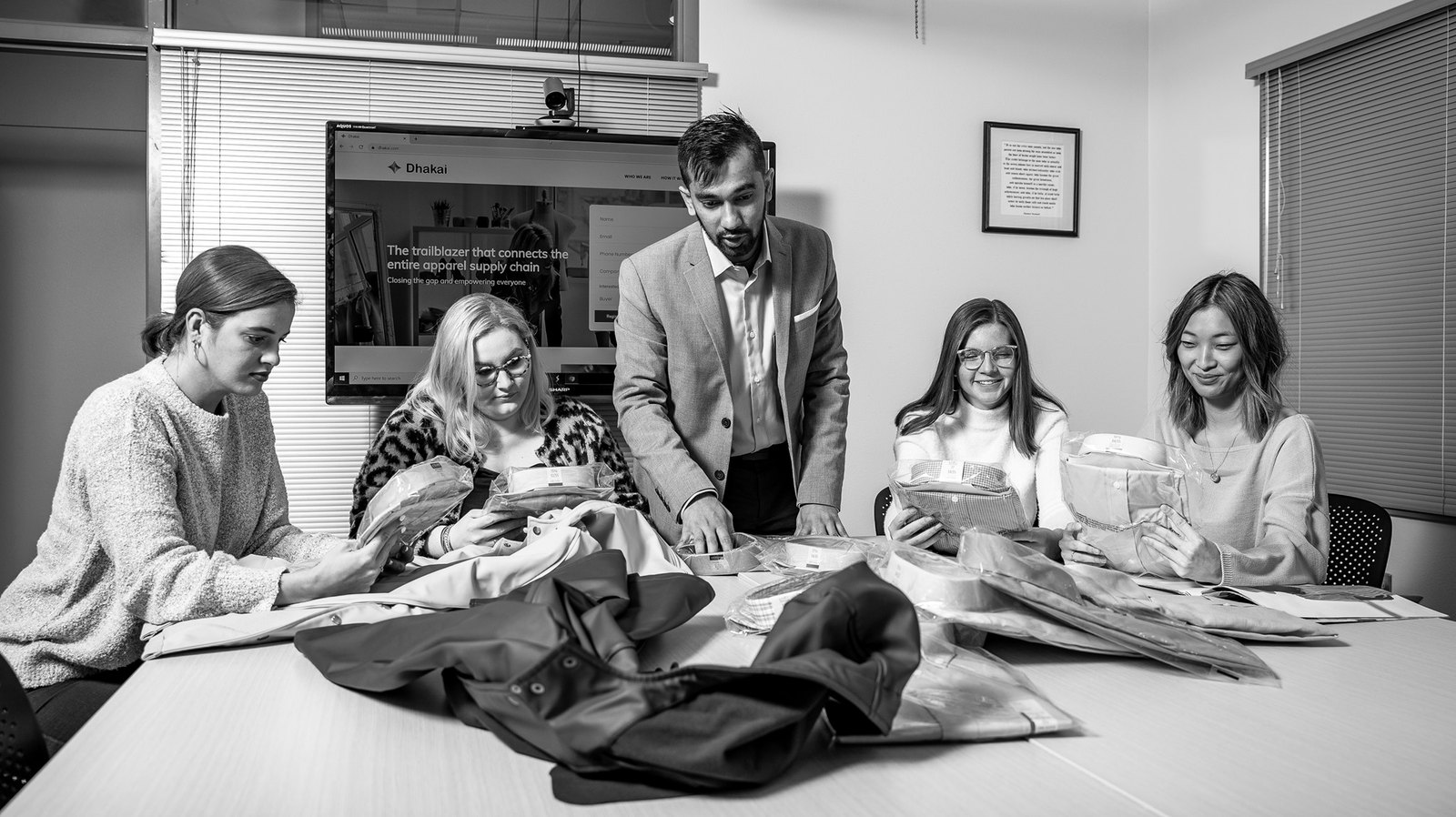 Russel Karim standing at a conference table as four colleagues inspect shirts and fabric samples