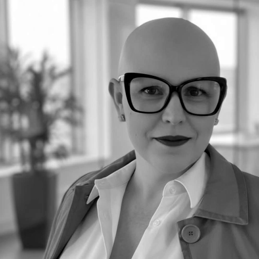 Laura Cole in bold dark glasses and a collared shirt, smiling at the camera