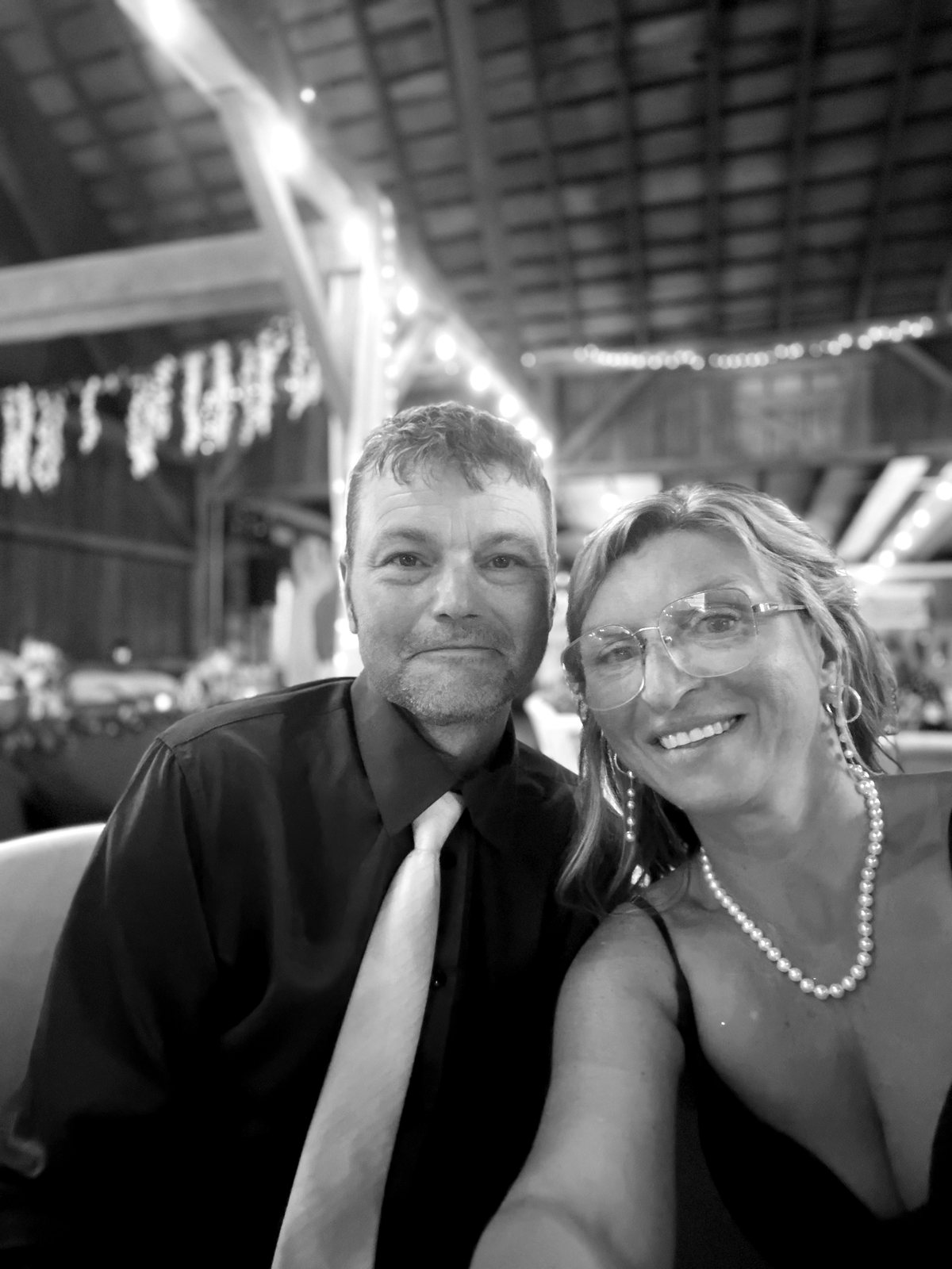 Janae Ohrt and her husband smiling together at a family wedding in a barn strung with lights