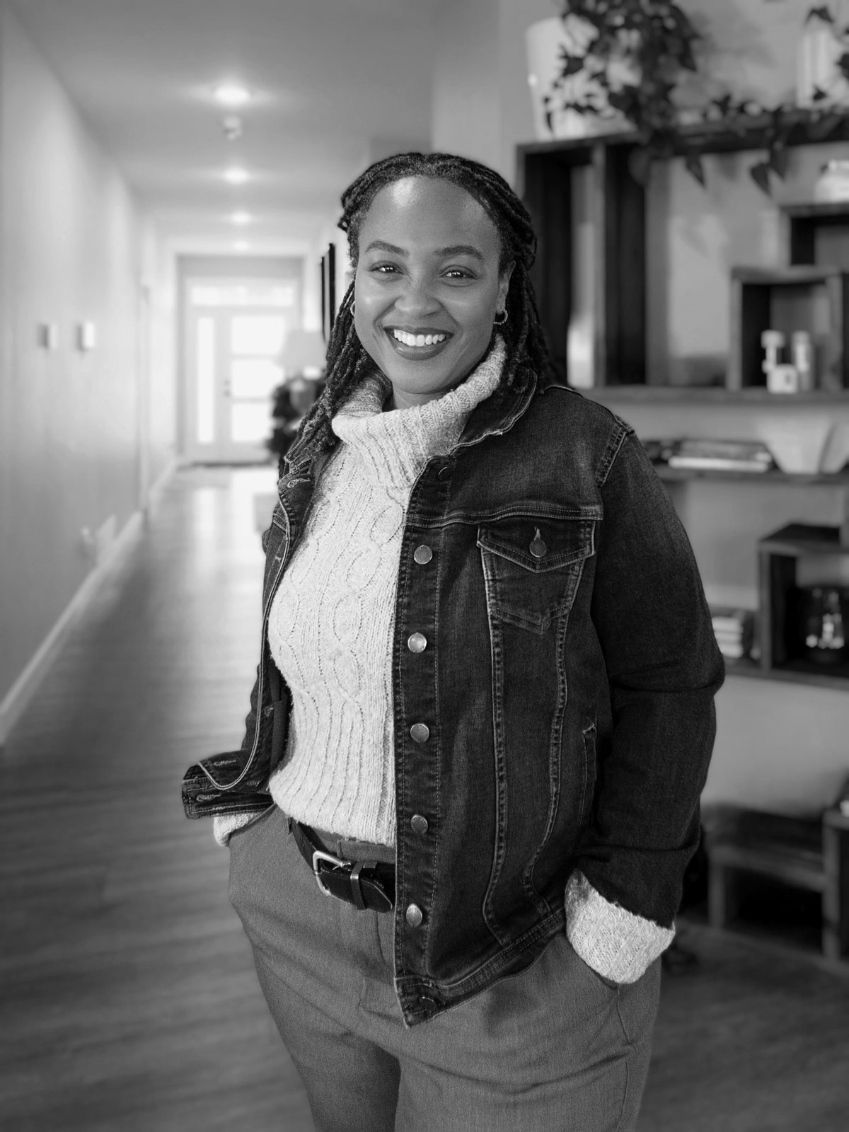 Melanie Myles smiling in a denim jacket and cable-knit sweater, hands in her pockets, in a hallway at home